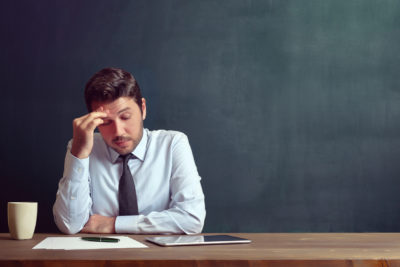 Teacher Looking Stressed at a Tablet on His Desk