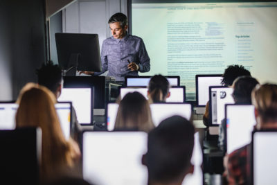 Mid adult professor teaching a lecture from desktop PC at computer lab