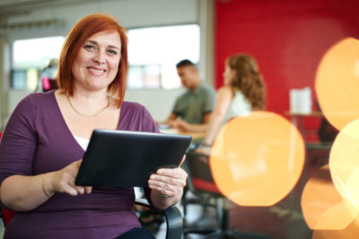 Female educator in front of a classroom holding a tablet